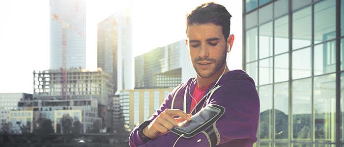 Um homem praticante de atividade física, mexendo no celular que está preso ao braço