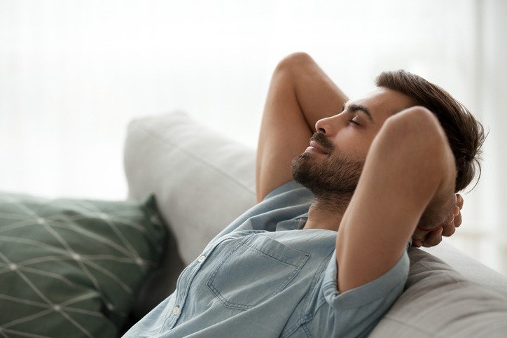 Homem com camisa jeans descansa de olhos fechados sentado no sofa
