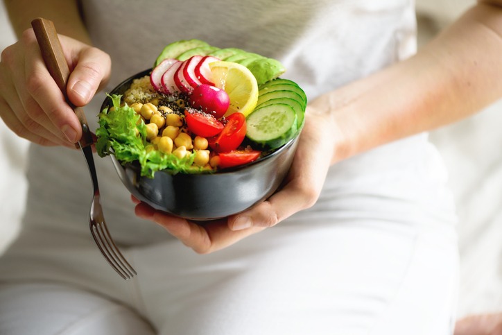 Mãos de uma mulher com roupa branca seguram uma tigela de salada