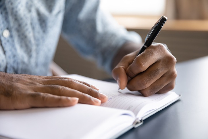 Mãos masculinas apoiadas em um caderno escrevendo com uma caneta