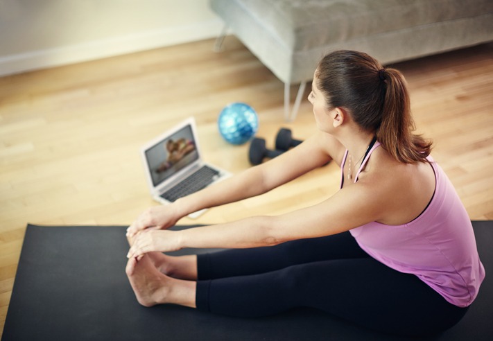 Mulher faz exercício em tapete de ioga enquanto acompanha as instruções pelo notebook