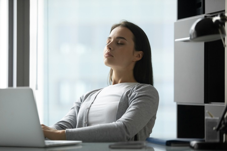 Mulher de olhos fechados respira fundo para aliviar o estresse do trabalho