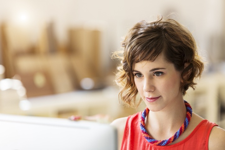 Mulher de cabelo curto e moderno olha concentrada para a tela do computador