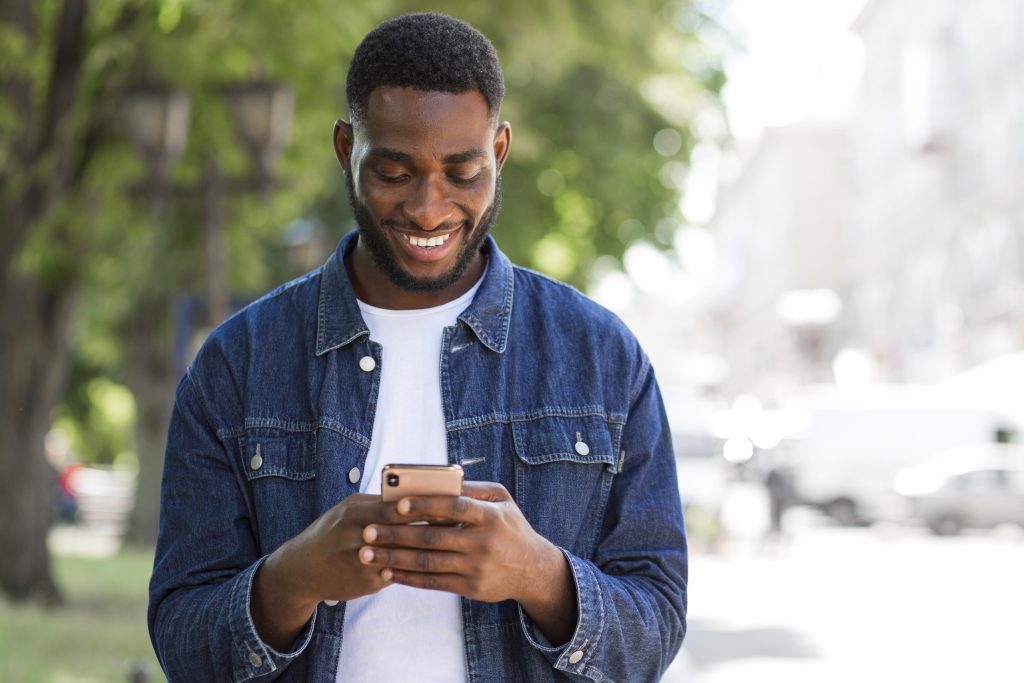Homem sorridente mexendo no celular na rua